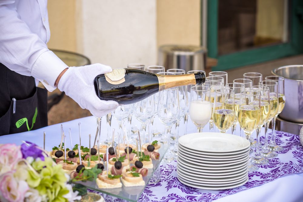 Hand of the waiter pours white wine in wineglass. Bright picture of pouring wine into glasses.